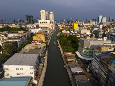 Bangkok Thailand 26 April 2026 Aerial view of a long canal flowing through dense urban neighborhoods with modern skyscrapers and high rise buildings in the background.