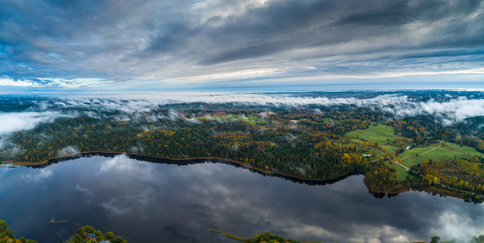 Aerial view of a serene lake surrounded by autumn forests and green fields under a dramatic cloudy sky in Latvia. Aerial view of a serene lake surrounded by autumn forests and green fields under a dramatic cloudy sky in Latvia.