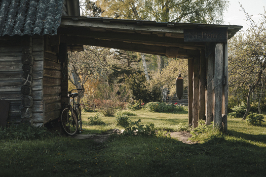 Laane County Estonia 19 May 2025 View of a rustic wooden log shed with a bicycle leaning against the wall and a hanging buoy in a lush garden on Vormsi island.