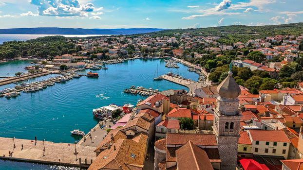 Aerial view of the historic town of Krk featuring a prominent church bell tower terracotta rooftops and a harbor filled with boats Krk Primorje Gorski Kotar Croatia.