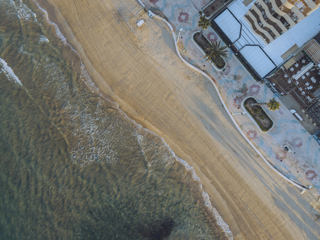 Aerial view of the sandy beach and patterned promenade with palm trees and buildings in Calp Valencian Community Spain. Aerial view of the sandy beach and patterned promenade with palm trees and buildings in Calp Valencian Community Spain.
