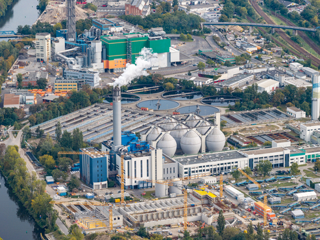 Aerial view of Klarwerk Ruhleben sewage treatment plant featuring circular tanks a tall chimney with smoke and industrial infrastructure along the river in Berlin Berlin Germany.