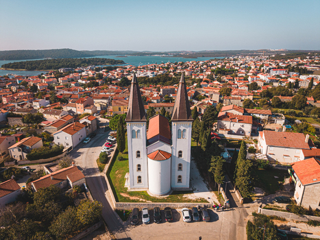 Aerial view of a serene church standing tall amidst the terracotta rooftops and the shimmering Adriatic sea in the backdrop Medulin Istria County Croatia.
