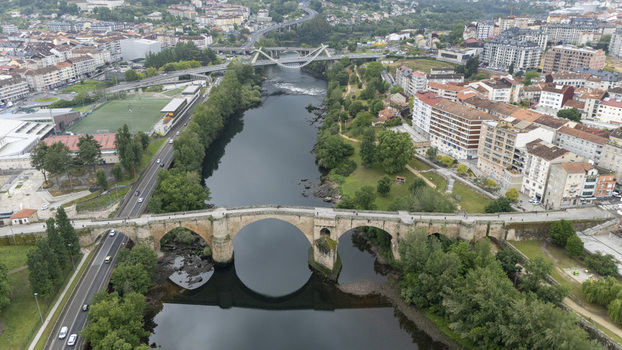 Aerial view of the historic Ponte Vella de Ourense stone bridge spanning the Minho River surrounded by lush green trees and urban cityscape in Ourense Ourense Spain.