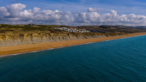 Aerial view of West Bay with its iconic golden sandstone cliffs sandy beach and holiday park nestled on the coastline in West Bay England United Kingdom. Aerial view of West Bay with its iconic golden sandstone cliffs sandy beach and holiday park nestled on the coastline in West Bay England United Kingdom.