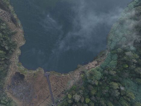 Aerial view of the misty Dieng lake surrounded by lush forest and a wooden pier extending into the dark water in Kejajar Central Java Indonesia. Aerial view of the misty Dieng lake surrounded by lush forest and a wooden pier extending into the dark water in Kejajar Central Java Indonesia.