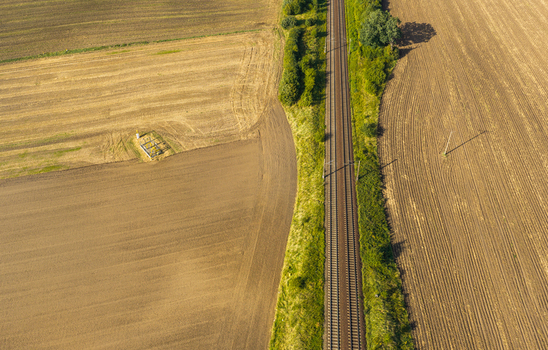 Aerial view of railway tracks cutting through agricultural fields with brown soil and green vegetation in Pomeranian Voivodeship Poland.