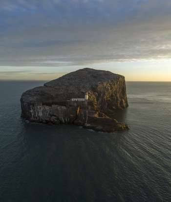 Aerial view of Bass Rock Lighthouse perched on the steep volcanic cliffs of Bass Rock island during golden hour in North Berwick Scotland United Kingdom. Aerial view of Bass Rock Lighthouse perched on the steep volcanic cliffs of Bass Rock island during golden hour in North Berwick Scotland United Kingdom.