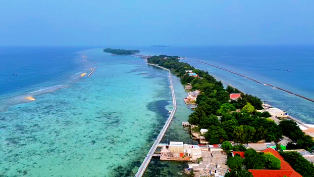 Aerial view of Pulau Tidung Besar with its iconic long wooden bridge surrounded by vibrant turquoise coral reefs and tropical vegetation in South Kepulauan Seribu Jakarta Indonesia.