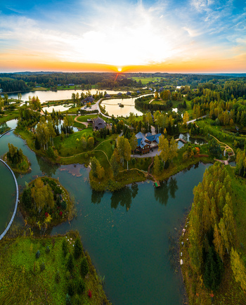 Aerial view of a serene landscape featuring interconnected lakes lush green forests and wooden buildings during a golden sunset in Latvia. Aerial view of a serene landscape featuring interconnected lakes lush green forests and wooden buildings during a golden sunset in Latvia.