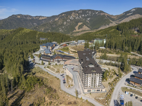 Aerial view of modern hotel complexes and mountain resorts nestled among dense pine forests and rolling hills under a clear blue sky in Demanovska Dolina Zilina Region Slovakia.