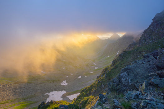 View of Smutne sedlo in Western Tatras with golden sunset light piercing through dense fog over rocky slopes and patches of snow in Ziar Zilina Region Slovakia. View of Smutne sedlo in Western Tatras with golden sunset light piercing through dense fog over rocky slopes and patches of snow in Ziar Zilina Region Slovakia.