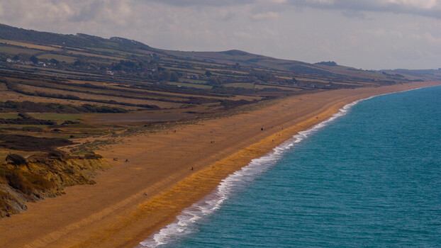 Aerial view of the coastline at West Bay with golden sandy beach turquoise sea and rolling green hills of the Jurassic Coast in West Bay England United Kingdom. Aerial view of the coastline at West Bay with golden sandy beach turquoise sea and rolling green hills of the Jurassic Coast in West Bay England United Kingdom.