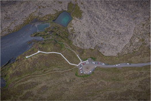 Aerial view of the parking area and walking path leading to the black sand beach of Djupalonssandur surrounded by volcanic terrain and small ponds in Iceland. Aerial view of the parking area and walking path leading to the black sand beach of Djupalonssandur surrounded by volcanic terrain and small ponds in Iceland.