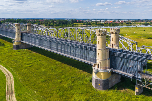 Aerial view of the historic Tczew Bridge with its distinctive towers spanning the Vistula River surrounded by green meadows under a blue sky in Tczew Pomeranian Voivodeship Poland. Aerial view of the historic Tczew Bridge with its distinctive towers spanning the Vistula River surrounded by green meadows under a blue sky in Tczew Pomeranian Voivodeship Poland.