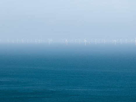 Aerial view of an offshore wind farm with rows of white wind turbines standing in the blue sea under a hazy sky in Plurien Brittany France. Aerial view of an offshore wind farm with rows of white wind turbines standing in the blue sea under a hazy sky in Plurien Brittany France.
