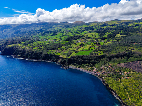 Aerial view of the jagged coastline meeting the deep blue sea with the verdant hills of Miradouro Prainha stretching into the cloudy horizon Pico Azores Portugal. Aerial view of the jagged coastline meeting the deep blue sea with the verdant hills of Miradouro Prainha stretching into the cloudy horizon Pico Azores Portugal.