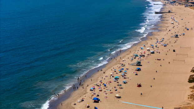 Aerial view of Will Rogers State Beach with people relaxing on the sand colorful umbrellas and gentle waves rolling onto the shore in Los Angeles California United States.