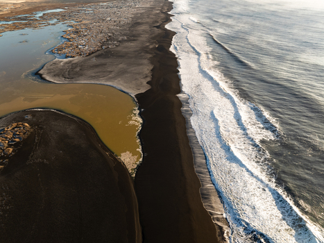 Aerial view of the dramatic black sand beach meeting the Atlantic Ocean with waves crashing against the shore and a calm lagoon nearby in Reykjanesbaer Iceland. Aerial view of the dramatic black sand beach meeting the Atlantic Ocean with waves crashing against the shore and a calm lagoon nearby in Reykjanesbaer Iceland.
