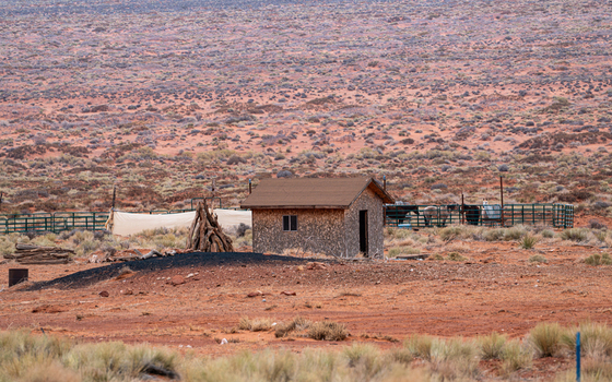 View of a stone cabin in the arid desert landscape of Monument Valley Tribal Park with horses in a corral and red earth in Oljato Monument Valley Utah United States.