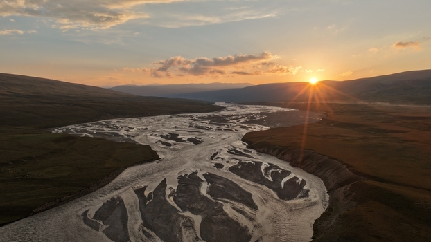 Aerial view of the braided Enilchek River winding through the mountainous landscape at sunset with golden light on the water Enilchek Issyk Kul Region Kyrgyzstan. Aerial view of the braided Enilchek River winding through the mountainous landscape at sunset with golden light on the water Enilchek Issyk Kul Region Kyrgyzstan.