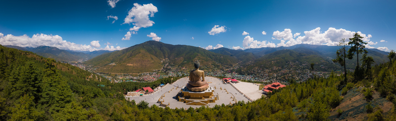 Aerial panorama view of the golden Great Buddha Dordenma statue sitting atop a vast plaza embraced by green mountains and a bright sky Thimphu Bhutan.