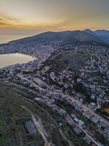 Aerial view of the coastal city of Saranda at sunset featuring the bay urban buildings and surrounding hills in Saranda Vlore County Albania. Aerial view of the coastal city of Saranda at sunset featuring the bay urban buildings and surrounding hills in Saranda Vlore County Albania.