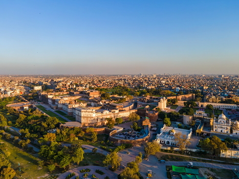 Aerial view of the historic Lahore Fort complex with its ancient walls courtyards and surrounding lush gardens under a clear blue sky in Lahore Punjab Pakistan.