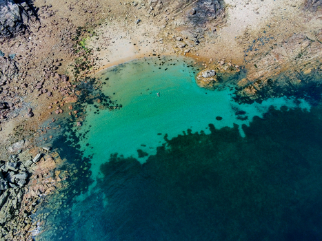 Aerial view of the turquoise waters of a small sandy cove at Brehat surrounded by rugged rocky coastline and clear sea in Ile de Brehat Brittany France.
