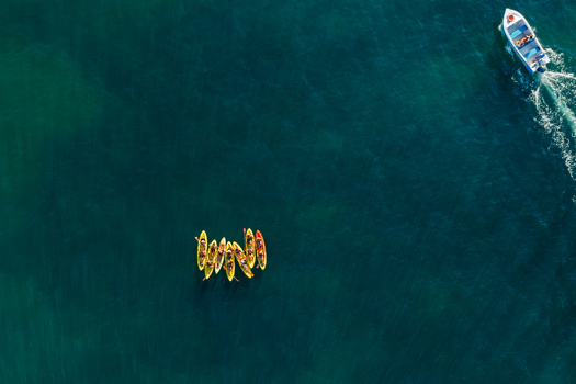Aerial view of a group of yellow kayaks with people paddling in the deep blue ocean near a small motorboat in Lagos Faro District Portugal.
