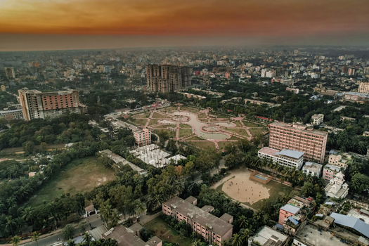 Chattogram Chittagong Division Bangladesh 06 January 2022 Aerial view of the city landscape with a central park pond dense buildings and a warm sunset sky.