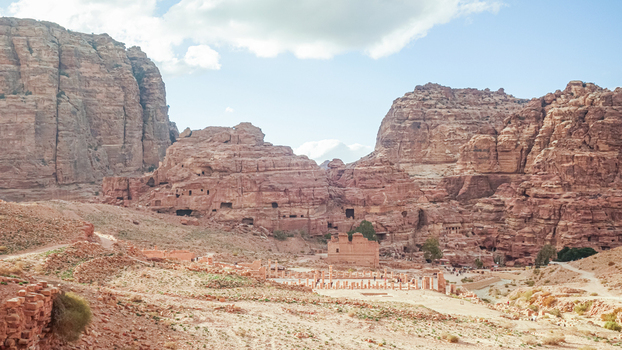 View of the ancient archaeological site of Petra with red sandstone cliffs rocky desert terrain and historic ruins under a bright sky in Wadi Musa Ma an Governorate Jordan. View of the ancient archaeological site of Petra with red sandstone cliffs rocky desert terrain and historic ruins under a bright sky in Wadi Musa Ma an Governorate Jordan.