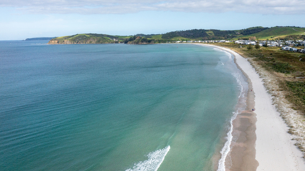 Aerial view of Omaha Beach with turquoise waters white sand and coastal hills in Omaha Auckland New Zealand.