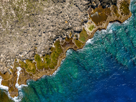 Aerial view of Chigit Beach featuring rugged limestone cliffs and vibrant turquoise waters along the coastline of Northern Tinian Tinian Northern Mariana Islands. Aerial view of Chigit Beach featuring rugged limestone cliffs and vibrant turquoise waters along the coastline of Northern Tinian Tinian Northern Mariana Islands.
