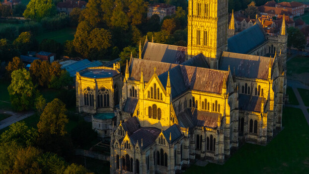 Aerial view of Salisbury Cathedral illuminated by golden sunset light showcasing its Gothic architecture stone spires and surrounding green grounds in Salisbury England United Kingdom. Aerial view of Salisbury Cathedral illuminated by golden sunset light showcasing its Gothic architecture stone spires and surrounding green grounds in Salisbury England United Kingdom.
