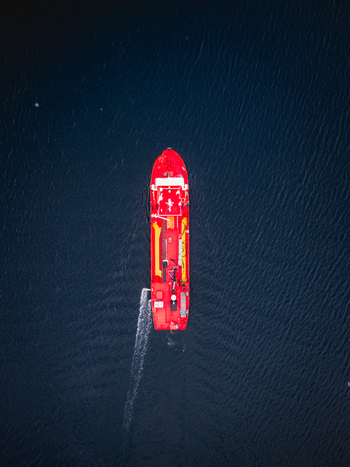 Aerial view of a vibrant red boat slicing through the dark textured waters off the coast Ballstad Nordland Norway. Aerial view of a vibrant red boat slicing through the dark textured waters off the coast Ballstad Nordland Norway.
