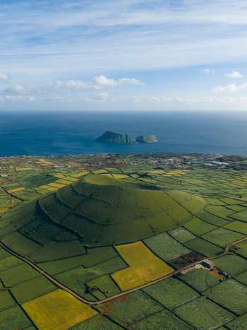 Aerial view of the volcanic cone Pico Dona Joana surrounded by a patchwork of green agricultural fields and the Atlantic Ocean in the background Feteira Acores Portugal.