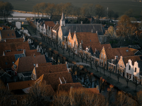 Aerial view of historic red tiled rooftops and a traditional church along a canal during golden hour in Sloten Friesland Netherlands. Aerial view of historic red tiled rooftops and a traditional church along a canal during golden hour in Sloten Friesland Netherlands.