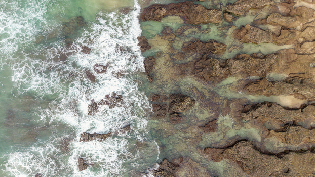 Aerial view of ocean waves crashing against the rocky shoreline of Hartenbos beach in Mossel Bay Western Cape South Africa. Aerial view of ocean waves crashing against the rocky shoreline of Hartenbos beach in Mossel Bay Western Cape South Africa.