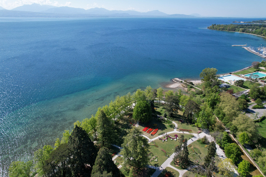Aerial view of the lush Parc de l Independance with colorful flower beds and green trees along the shores of Lake Geneva with mountains in the background in Morges Vaud Switzerland. Aerial view of the lush Parc de l Independance with colorful flower beds and green trees along the shores of Lake Geneva with mountains in the background in Morges Vaud Switzerland.