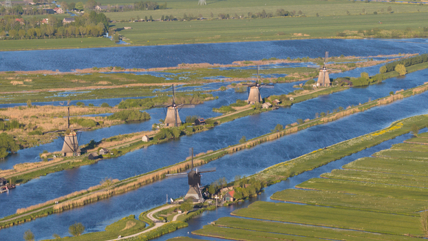 Aerial view of historic windmills standing along narrow canals and lush green polders under bright sunlight Kinderdijk South Holland Netherlands. Aerial view of historic windmills standing along narrow canals and lush green polders under bright sunlight Kinderdijk South Holland Netherlands.