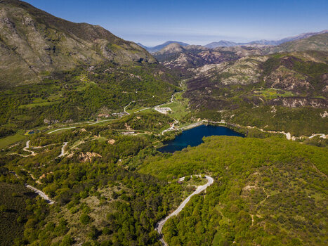 Aerial view of Blue Eye surrounded by lush green forests winding roads and rugged mountains in the landscape of Finiq Vlore County Albania. Aerial view of Blue Eye surrounded by lush green forests winding roads and rugged mountains in the landscape of Finiq Vlore County Albania.