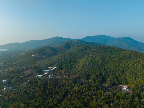 Aerial view of Karimunjawa hills covered in dense tropical forest with a small village nestled at the base under a clear blue sky in Karimunjawa Central Java Indonesia. Aerial view of Karimunjawa hills covered in dense tropical forest with a small village nestled at the base under a clear blue sky in Karimunjawa Central Java Indonesia.