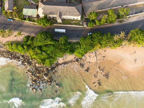 Aerial view of the coastline featuring a coastal road with traffic lush tropical trees and a sandy beach with rocky outcrops meeting the turquoise ocean waves in Galle Southern Province Sri Lanka.