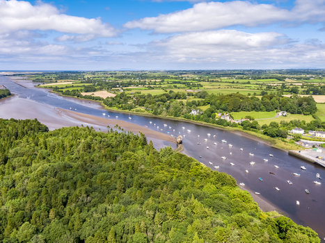 Aerial view of the River Moy flowing through the lush green landscape with small boats moored along the riverbanks under a bright blue sky in Ballina County Mayo Ireland.