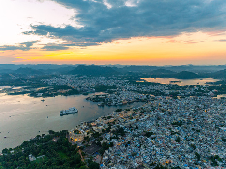 Aerial view of the City Palace and Lake Pichola during a vibrant sunset with golden light reflecting on the water and surrounding hills in Udaipur Rajasthan India.