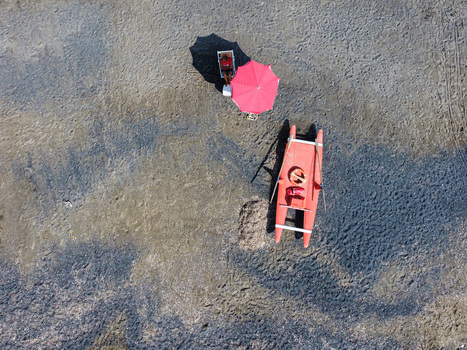 Aerial view of a lifeguard station on a sandy beach with a person under a red umbrella and a rescue boat in Imperia Liguria Italy. Aerial view of a lifeguard station on a sandy beach with a person under a red umbrella and a rescue boat in Imperia Liguria Italy.