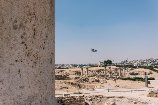 View of the ancient stone columns and ruins at the Amman Citadel with the Jordanian flag flying in the distance under a clear blue sky in Amman Amman Governorate Jordan.