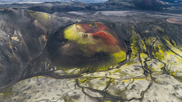 Aerial view of the vibrant Raudaskal crater with red and green moss covered slopes surrounded by dark volcanic terrain and rugged lava fields in Rangarthing ytra Iceland. Aerial view of the vibrant Raudaskal crater with red and green moss covered slopes surrounded by dark volcanic terrain and rugged lava fields in Rangarthing ytra Iceland.