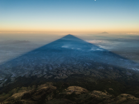 Aerial view of the triangular shadow cast by Gunung Sumbing Wonosobo over the landscape during sunrise with clouds and distant mountains in Kecamatan Kalikajar Jawa Tengah Indonesia.
